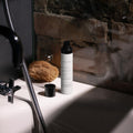 A bottle of Veluma moisturising day cream stands on a white bathroom counter next to its cap, with a sponge and a rustic brick wall in the background.